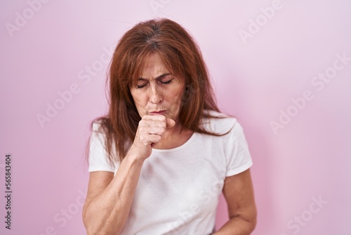 Middle age woman standing over pink background feeling unwell and coughing as symptom for cold or bronchitis. health care concept.
