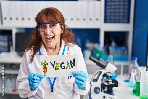 Middle age hispanic woman working at vegan laboratory smiling and laughing hard out loud because funny crazy joke.