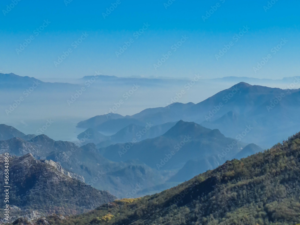 Panoramic view of dramatic karst mountain chains Dinaric Alps surrounding the Lake Skadar National Park seen from Goli Vrh, Montenegro, Balkan, Europe. Valley is covered by mystical fog, blue hills