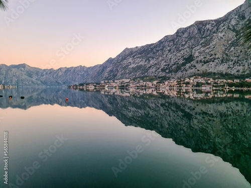 Panoramic view of bay of Kotor at twilight in summer, Adriatic Mediterranean Sea, Montenegro, Balkans, Europe. Fjord winding along coastal towns. First sunbeams on Lovcen mountains. Water reflection