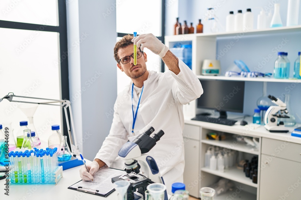 Young hispanic man scientist holding test tube write on document at laboratory Young hispanic man scientist holding test tube write on document at laboratory