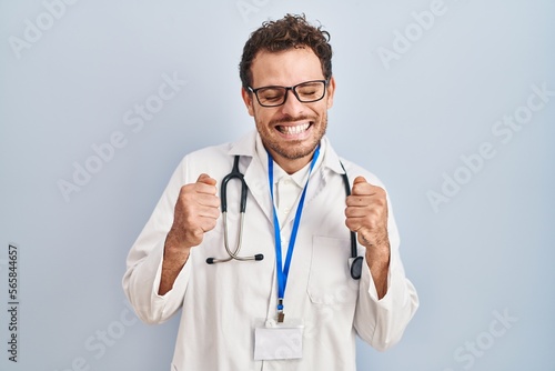 Young hispanic man wearing doctor uniform and stethoscope excited for success with arms raised and eyes closed celebrating victory smiling. winner concept.