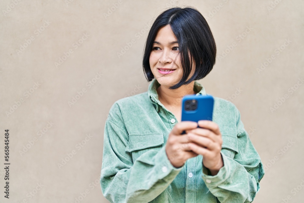 Fototapeta premium Young chinese woman smiling confident using smartphone at street