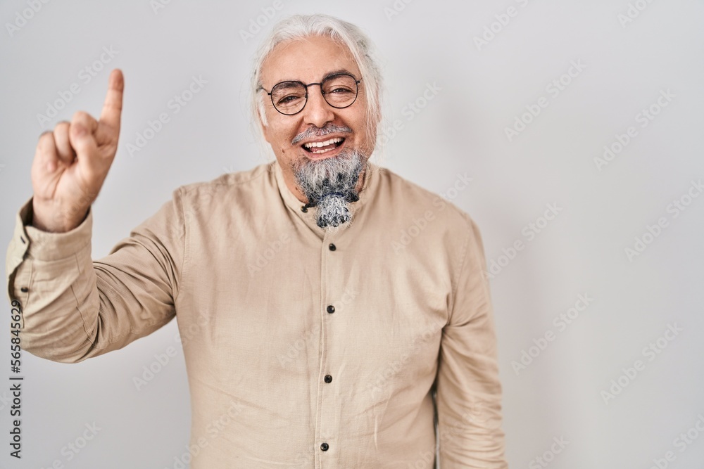 Middle age man with grey hair standing over isolated background showing and pointing up with finger number one while smiling confident and happy.