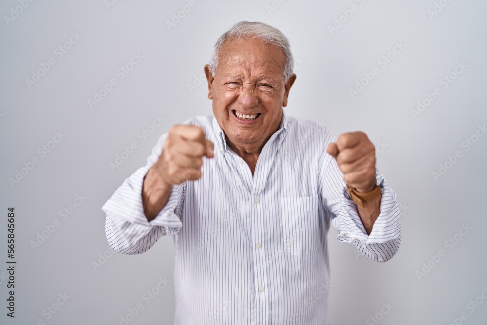 Senior man with grey hair standing over isolated background angry and mad raising fists frustrated and furious while shouting with anger. rage and aggressive concept. Senior man with grey hair standing over isolated background angry and mad raising fists frustrated and furious while shouting with anger. rage and aggressive concept.