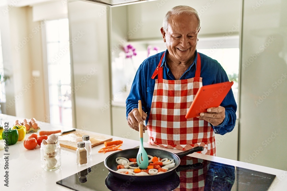 Senior man smiling confident cooking and watching online recipe at kitchen Senior man smiling confident cooking and watching online recipe at kitchen
