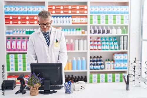 Middle age grey-haired man pharmacist smiling confident using computer at laboratory