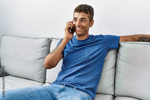 Young hispanic man relaxing sitting on the sofa speaking on the phone at home