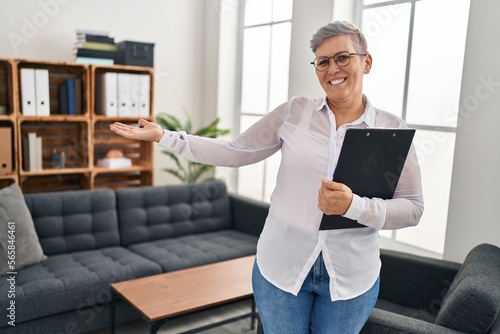 Middle age woman psychologist holding clipboard standing at pyschology center photo