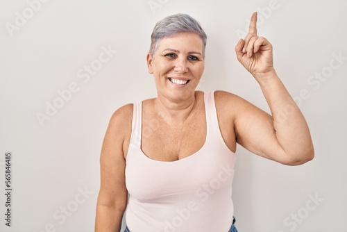 Middle age caucasian woman standing over white background pointing finger up with successful idea. exited and happy. number one.