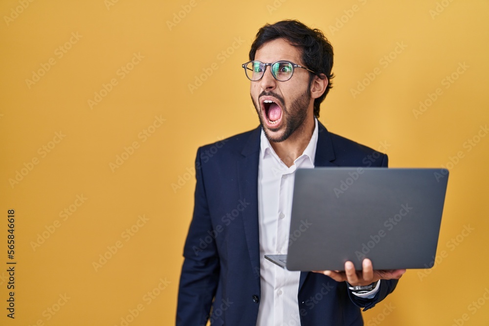 Handsome latin man working using computer laptop angry and mad screaming frustrated and furious, shouting with anger. rage and aggressive concept. Handsome latin man working using computer laptop angry and mad screaming frustrated and furious, shouting with anger. rage and aggressive concept.