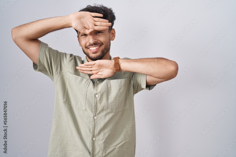 Arab man with beard standing over white background smiling cheerful playing peek a boo with hands showing face. surprised and exited Arab man with beard standing over white background smiling cheerful playing peek a boo with hands showing face. surprised and exited