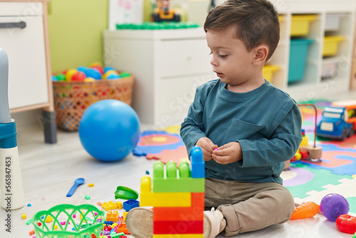 Adorable hispanic boy playing with construction blocks sitting on floor at kindergarten