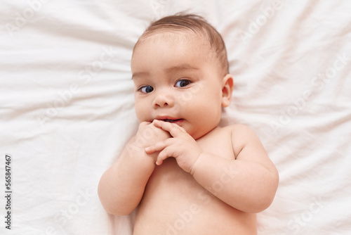 Adorable hispanic toddler lying on bed sucking finger at bedroom