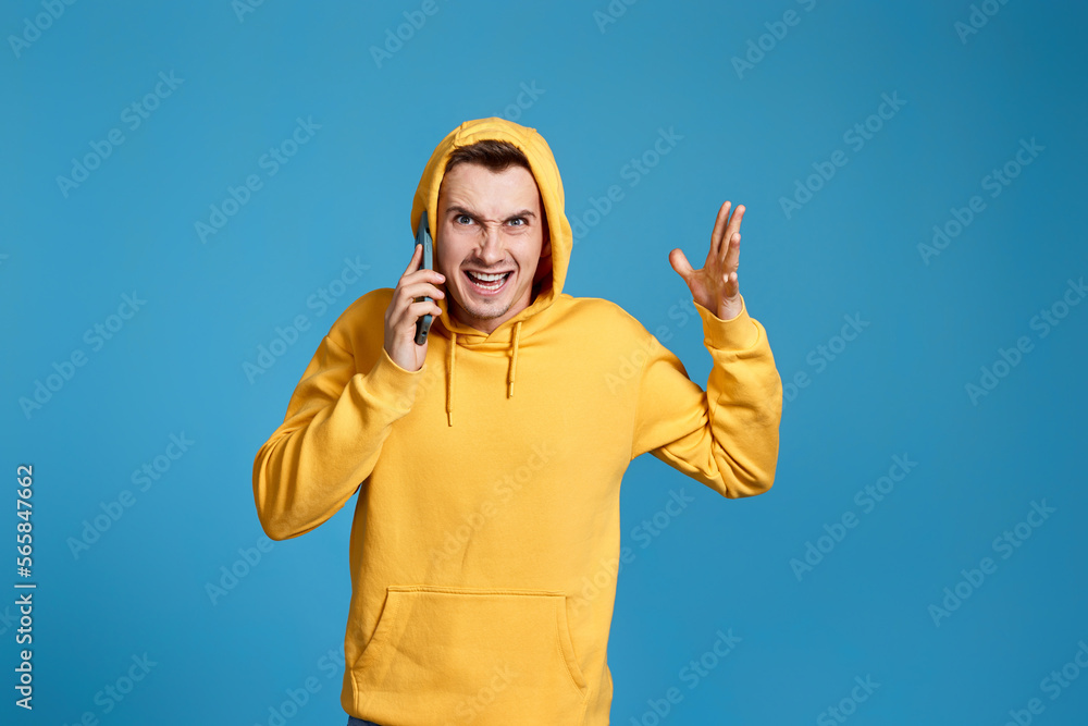 angry man in yellow sweatshirt holding mobile phone angry man in yellow sweatshirt holding mobile phone