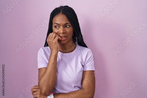 African american woman with braids standing over pink background looking stressed and nervous with hands on mouth biting nails. anxiety problem.