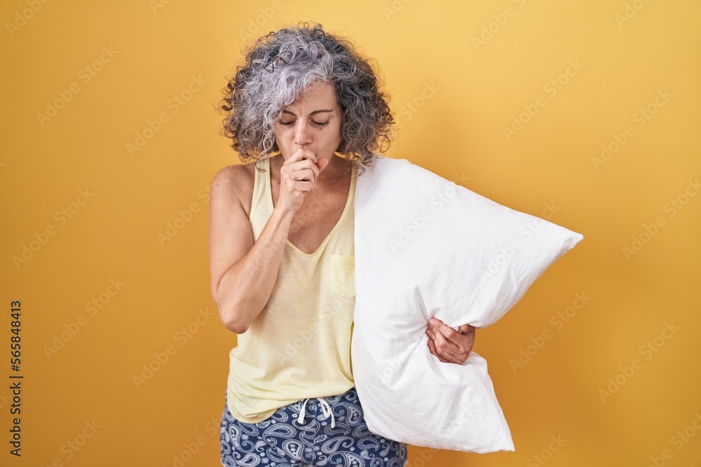 Middle age woman with grey hair wearing pijama hugging pillow feeling unwell and coughing as symptom for cold or bronchitis. health care concept. Middle age woman with grey hair wearing pijama hugging pillow feeling unwell and coughing as symptom for cold or bronchitis. health care concept.