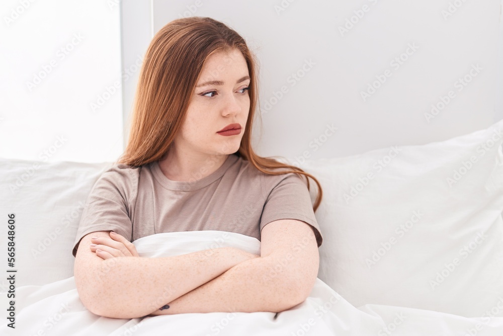 Young redhead woman sitting on bed with unhappy expression and arms crossed gesture at bedroom Young redhead woman sitting on bed with unhappy expression and arms crossed gesture at bedroom