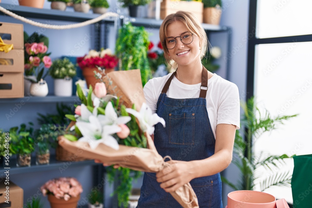 Young blonde girl florist holding bouquet of flowers at florist