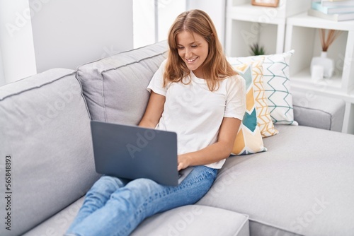 Young blonde girl using laptop sitting on sofa at home
