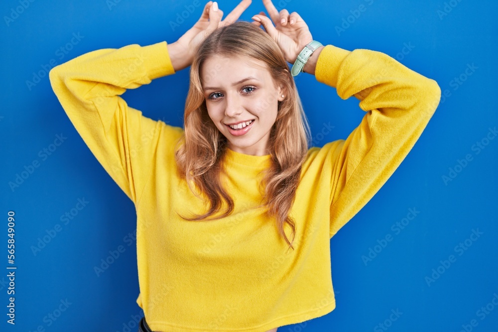 Young caucasian woman standing over blue background posing funny and crazy with fingers on head as bunny ears, smiling cheerful Young caucasian woman standing over blue background posing funny and crazy with fingers on head as bunny ears, smiling cheerful