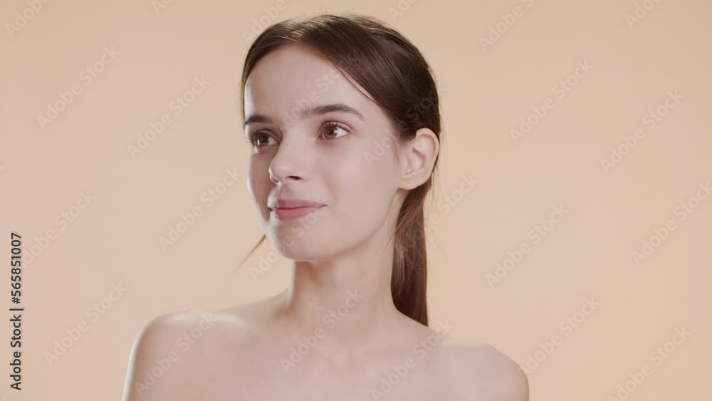 Gorgeous young slim Caucasian woman with long brown hair strokes her jawline and chin turning her head out of the camera smiling on beige background | Anti-acne concept Gorgeous young slim Caucasian woman with long brown hair strokes her jawline and chin turning her head out of the camera smiling on beige background | Anti-acne concept