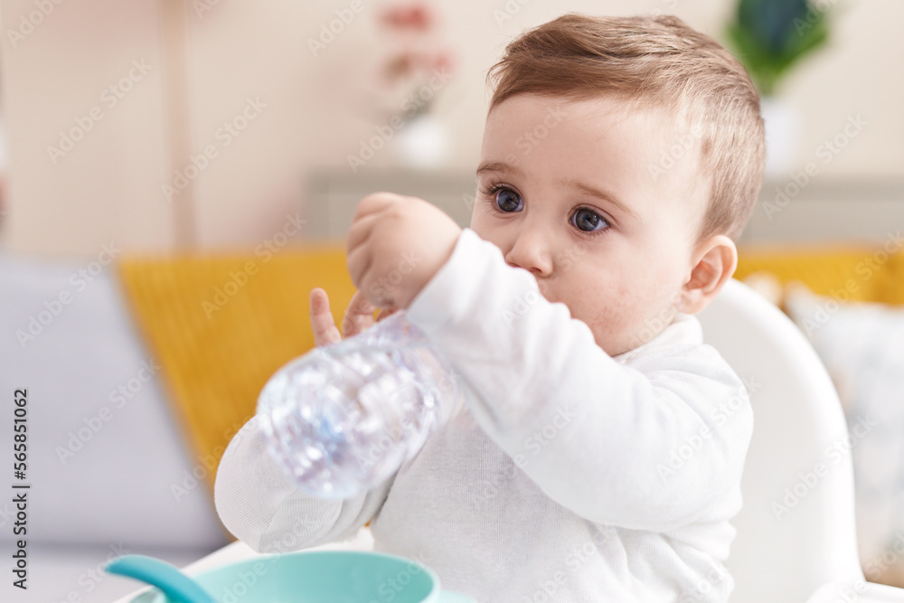 Adorable caucasian baby sitting on highchair drinking bottle of water at home Adorable caucasian baby sitting on highchair drinking bottle of water at home
