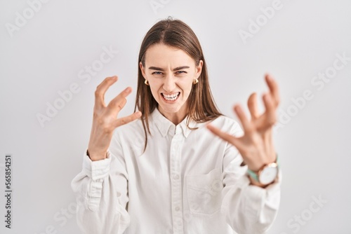 Young caucasian woman standing over isolated background shouting frustrated with rage, hands trying to strangle, yelling mad © Krakenimages.com