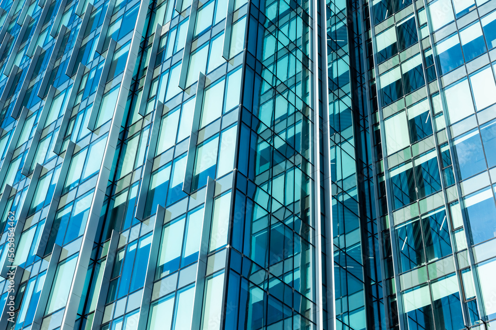 The blue sky is reflected in the windows of a modern office building. Architecture and exterior of contemporary houses