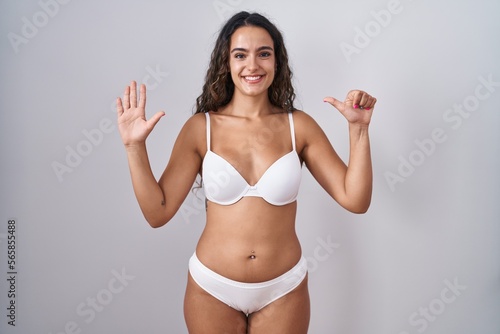 Young hispanic woman wearing white lingerie showing and pointing up with fingers number six while smiling confident and happy. © Krakenimages.com