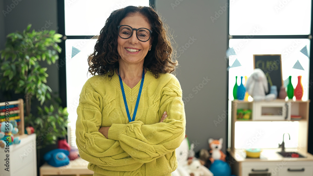 © Krakenimages.com - Middle age hispanic woman preschool teacher smiling confident standing with arms crossed gesture at kindergarten