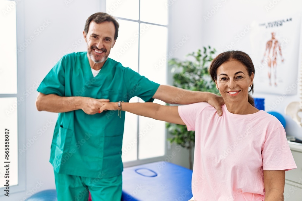 Obraz premium Middle age man and woman smiling confident stretching arm having rehab session at physiotherapy clinic