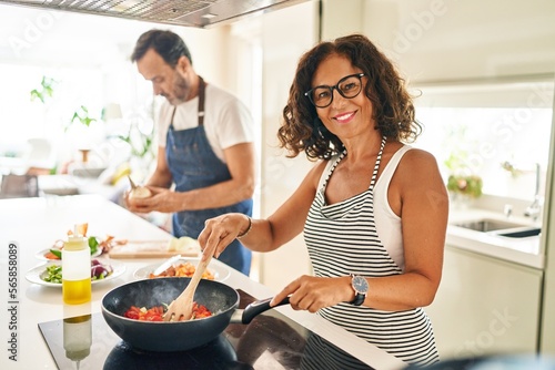 Middle age hispanic couple smiling confident cooking at kitchen