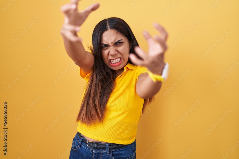 Young arab woman standing over yellow background shouting frustrated with rage, hands trying to strangle, yelling mad Young arab woman standing over yellow background shouting frustrated with rage, hands trying to strangle, yelling mad