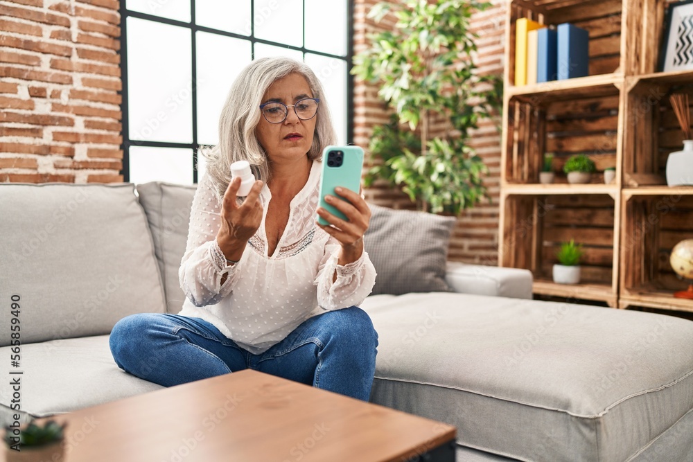 Obraz premium Middle age woman using smartphone holding pills at home