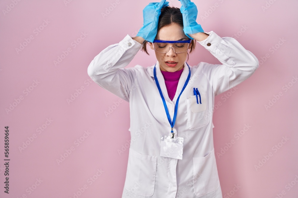 Hispanic woman wearing scientist uniform suffering from headache desperate and stressed because pain and migraine. hands on head. Hispanic woman wearing scientist uniform suffering from headache desperate and stressed because pain and migraine. hands on head.