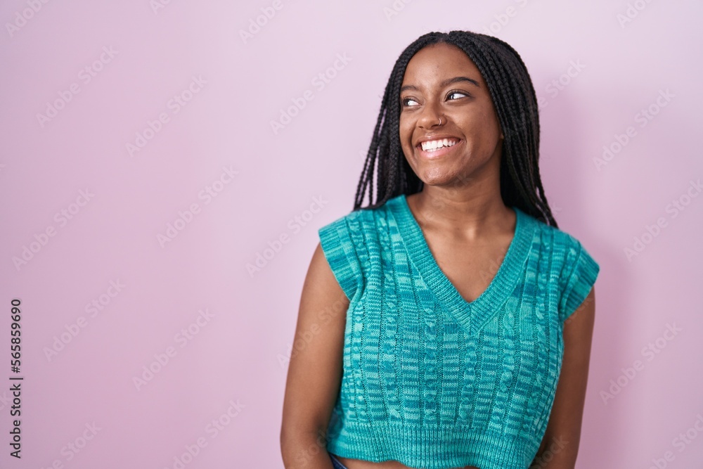 Young african american with braids standing over pink background looking away to side with smile on face, natural expression. laughing confident. Young african american with braids standing over pink background looking away to side with smile on face, natural expression. laughing confident.
