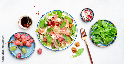 Freash salad with grape, jamon, blue cheese, arugula, nuts on white table background, top view, copy space