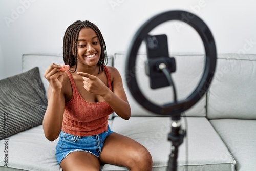 Young african american woman holding menstrual cup recording video tutorial at home