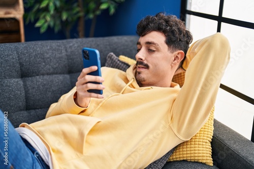 Young caucasian man using smartphone lying on sofa at home