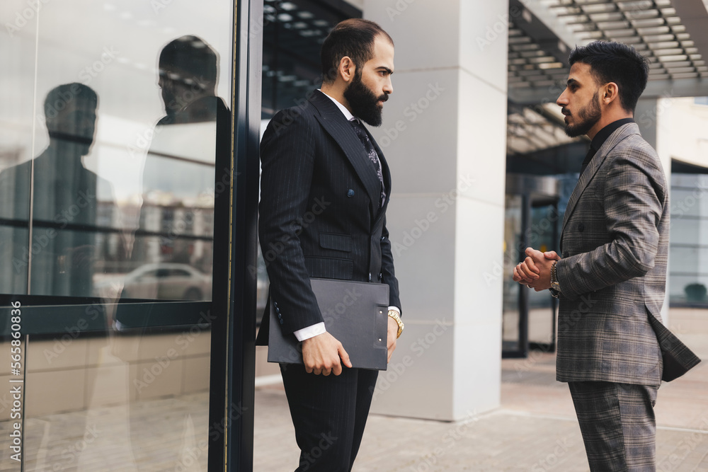 Business people outdoor meeting. Two men in suits are standing and talking to each other. Working break. Friendly conversation and business communication Business people outdoor meeting. Two men in suits are standing and talking to each other. Working break. Friendly conversation and business communication