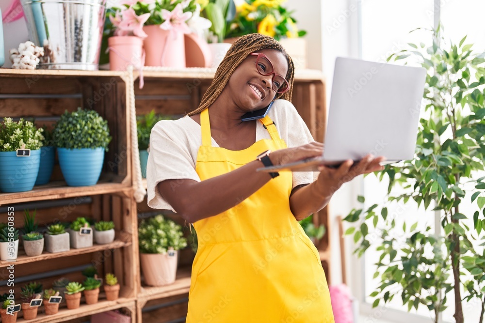 African american woman florist talking on smartphone using laptop at florist African american woman florist talking on smartphone using laptop at florist