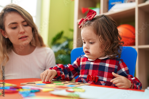 Teacher and toddler playing with maths puzzle game sitting on table at kindergarten