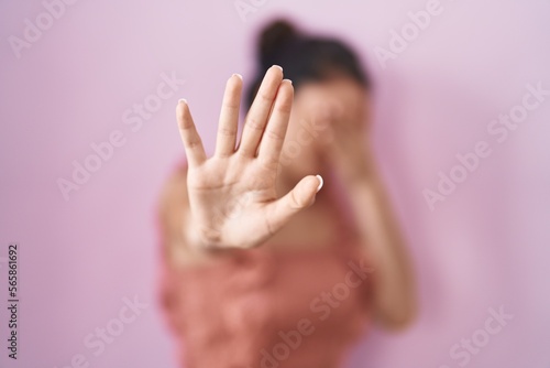 Young teenager girl standing over pink background covering eyes with hands and doing stop gesture with sad and fear expression. embarrassed and negative concept.