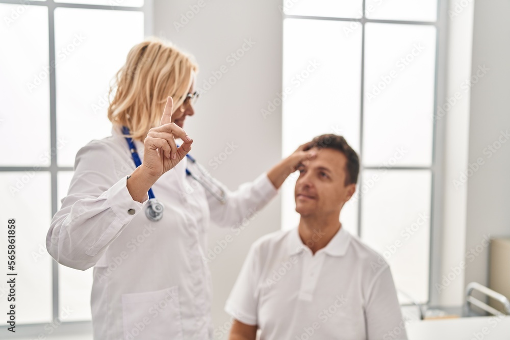 Fototapeta premium Middle age man and woman doctor and patient examining vision having medical consultation at clinic