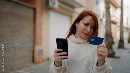 Young redhead woman using smartphone and credit card at street