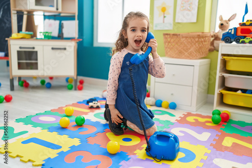 Adorable blonde girl playing with telephone toy sitting on floor at kindergarten photo