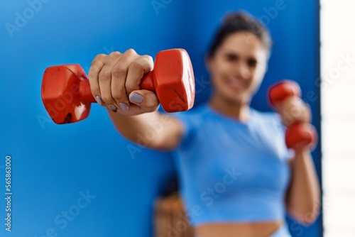 Young latin woman wearing sportswear boxing using dumbbells at sport center