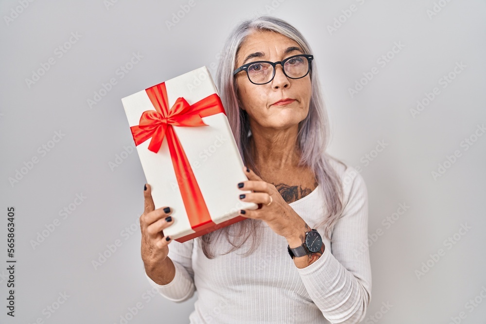 Middle age woman with grey hair holding gift relaxed with serious expression on face. simple and natural looking at the camera. Middle age woman with grey hair holding gift relaxed with serious expression on face. simple and natural looking at the camera.