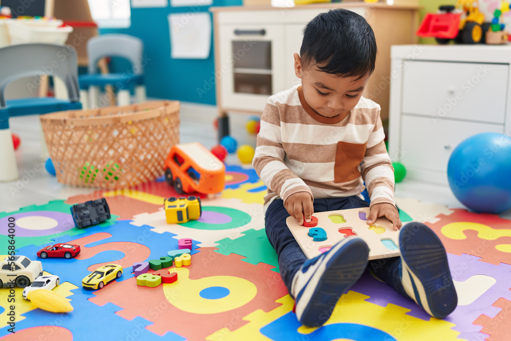 Adorable hispanic toddler playing with maths puzzle game sitting on floor at kindergarten Adorable hispanic toddler playing with maths puzzle game sitting on floor at kindergarten
